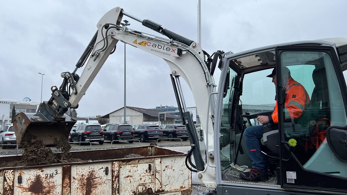 Mann schaufelt mit einem Bagger Sand in einen Container