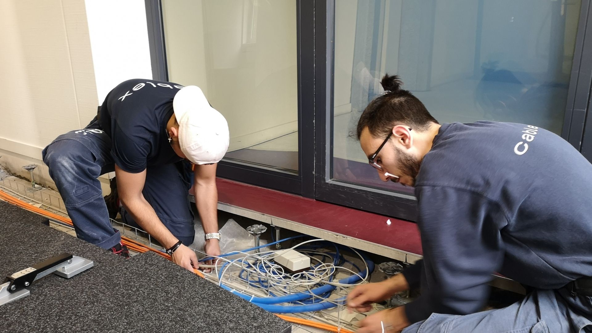 Two apprentice assembly electricians laying cable in a company building.