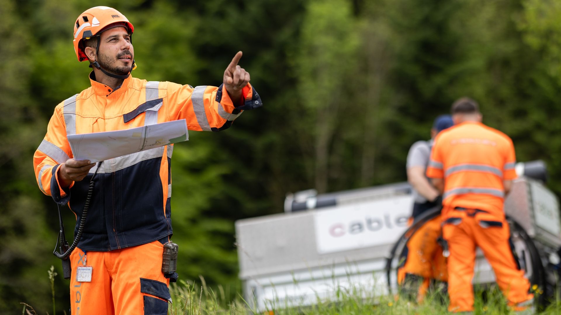cablex technician stands in the field, holding a construction plan and showing the team the task.