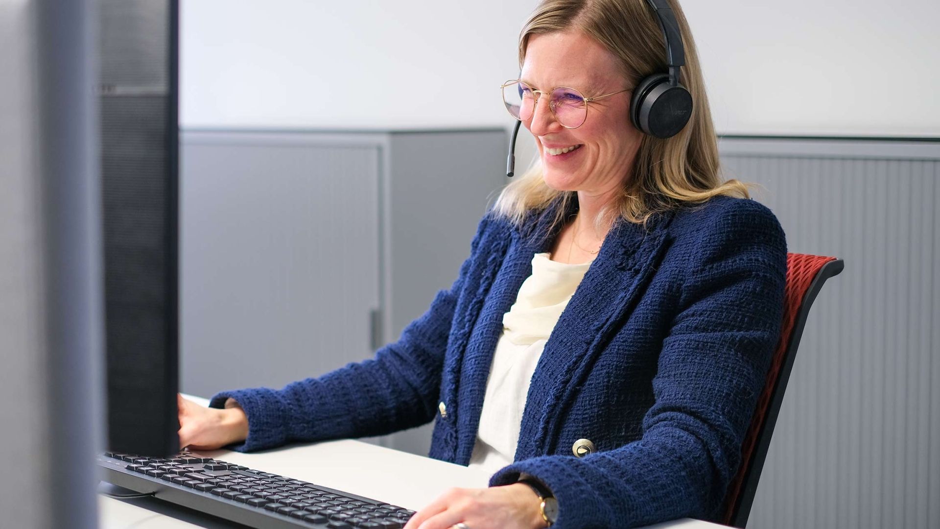 cablex Mitarbeitende mit Headset sitzt in einem Onlinemeeting und lächelt in die Webcam.