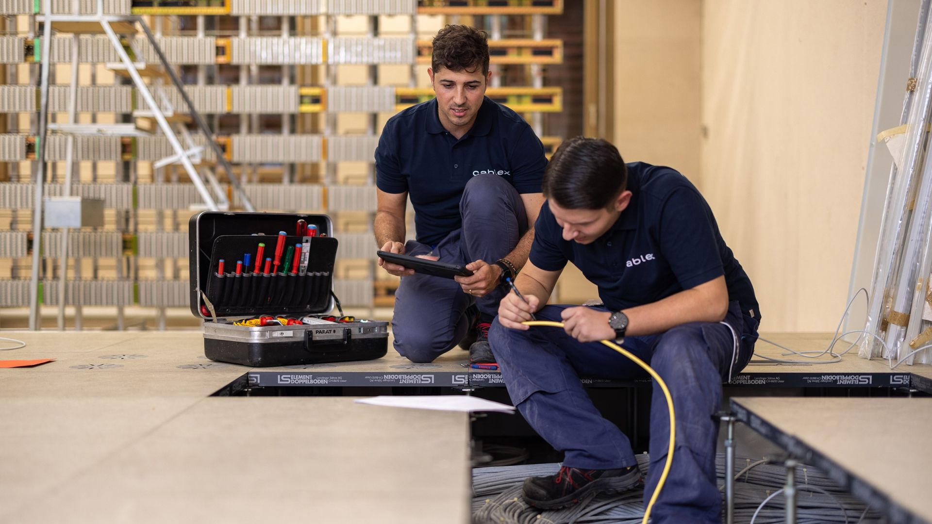 Two cablex technicians work on an electrical installation under the floor covering
