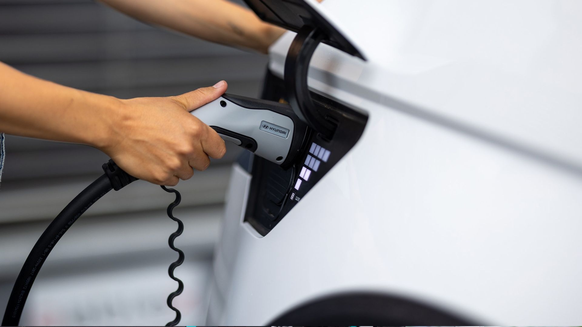 Nahaufnahme einer Person, die ihr Elektroauto an die E-Ladestation anschliesst