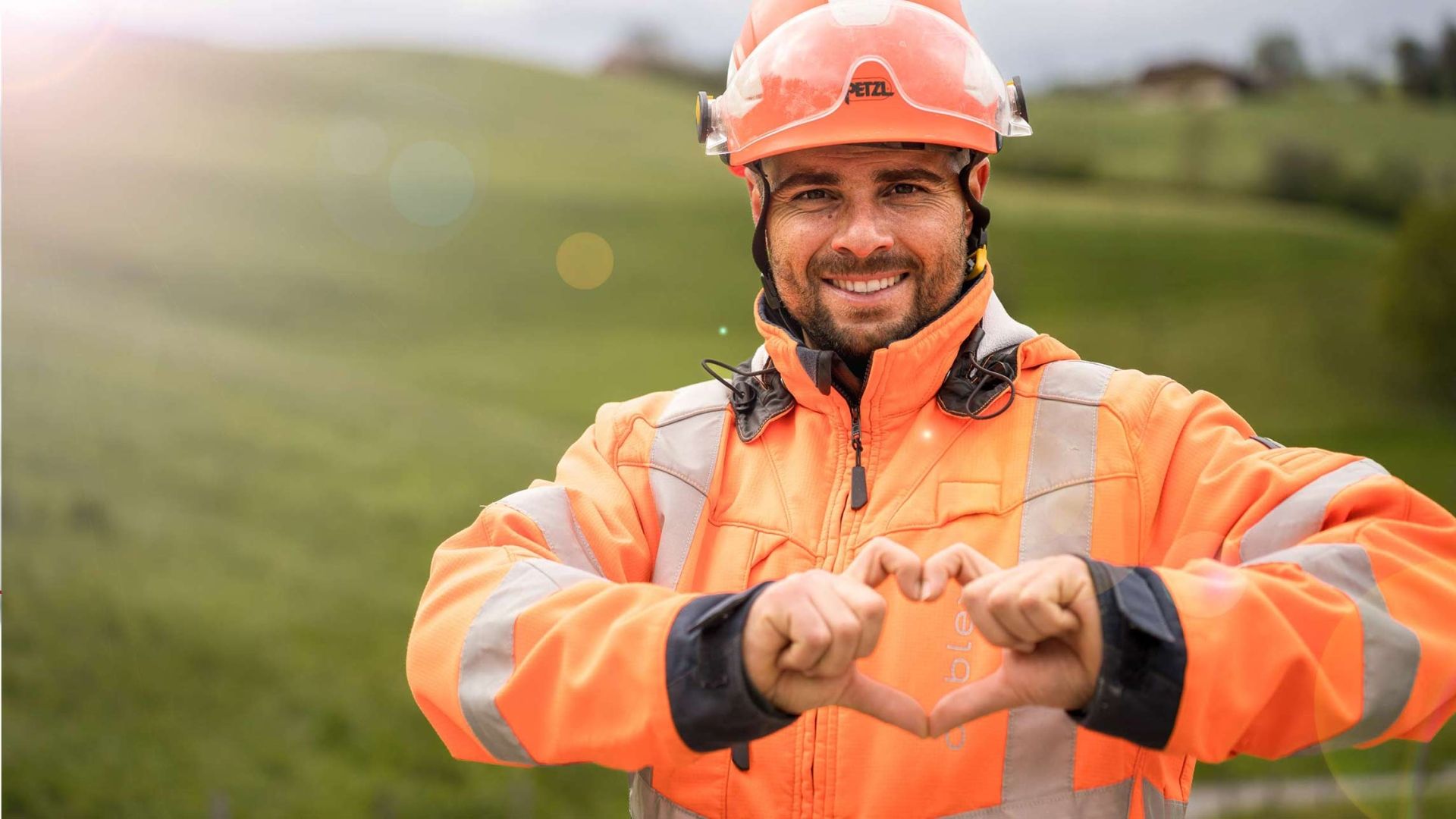 Un dipendente cablex si trova in un paesaggio verde e forma un cuore con le mani.