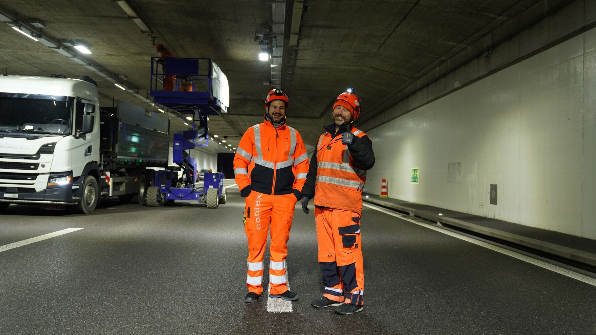 Zwei Männer in orangefarbener Schutzbekleidung stehen in einem Tunnel, der gerade saniert wird