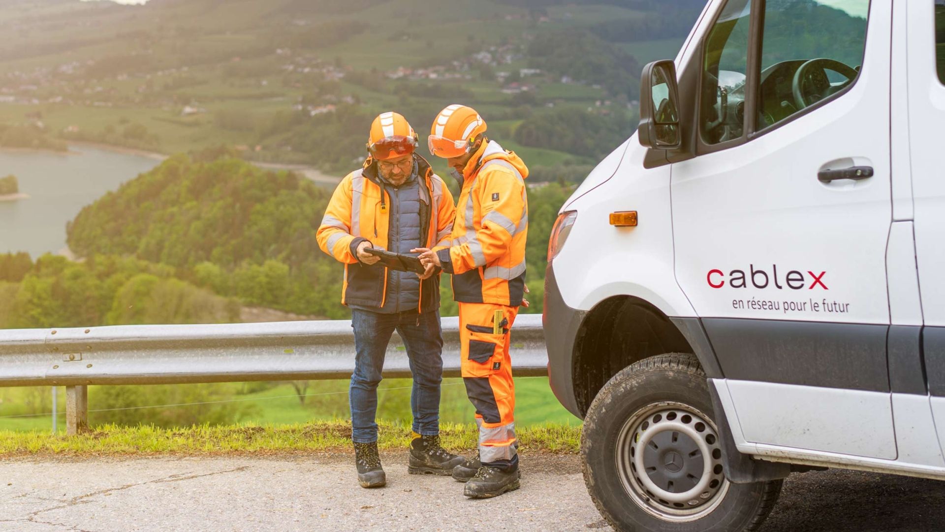 Due dipendenti cablex discutono di un progetto davanti a uno scenario suggestivo. Nell'immagine a destra si vede un veicolo cablex.