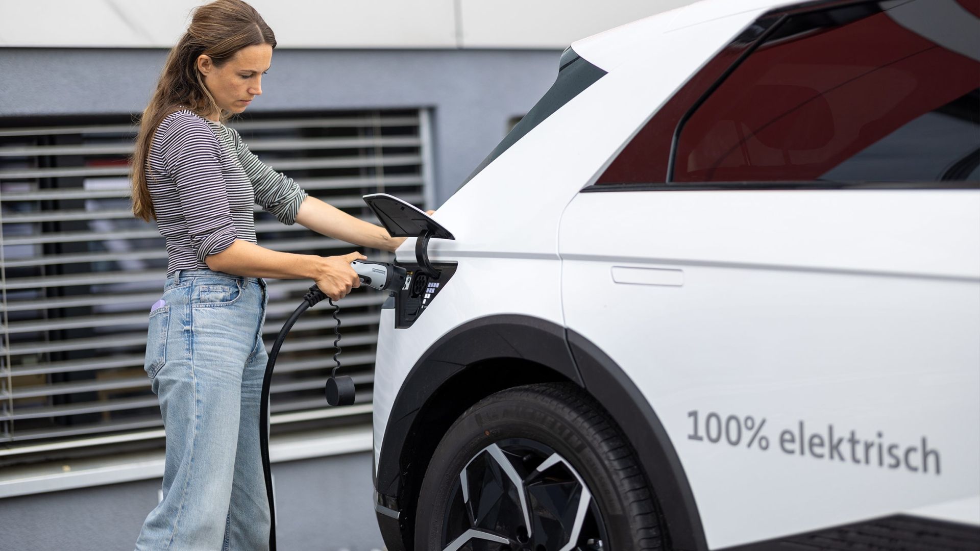 Frau steckt ihr Elektroauto an eine E-Ladestation