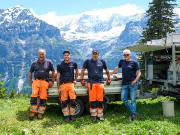 Four cablex technicians lean against car trailers with a mountain panorama in the background.