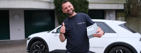 Field Service Techniker mit Smart Meter in der Hand vor seinem E-Auto