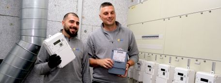 Zwei Techniker halten einen alten Stromzähler und einen neuen Smart Meter in den Händen.