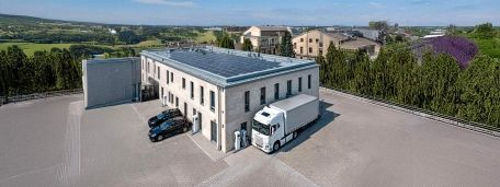 Elektrische PKW und ein elektrischer LKW vor einem Firmengebäude mit Ladestationen