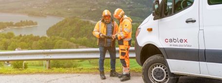 Two cablex employees discuss a project in a picturesque setting. A cablex vehicle is on the right.