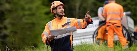Il tecnico cablex lavora sul campo, ha in mano un piano di costruzione e mostra al team il compito da svolgere.
