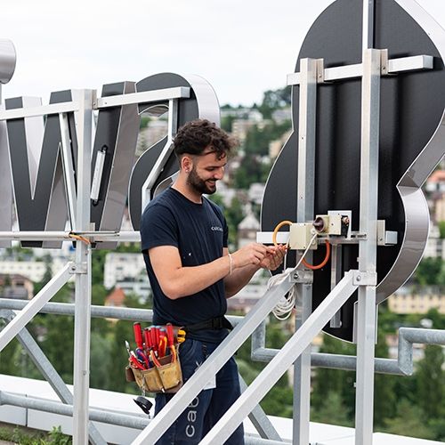 Apprenti installateur électrique travaillant sur l'installation électrique de Swisscom Logo.